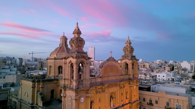 Cinematic 4K aerial vertical rise and tilt-down reveal of Msida Parish Church. Baroque architecture at sunset, Malta.