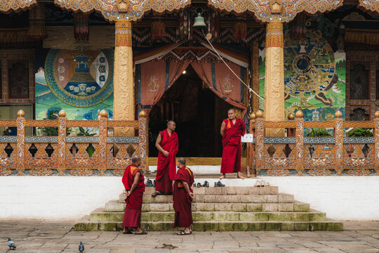 Punakha, Bhutan - 19 September 2025: View of crimson-robed monks congregating at the ornately decorated entrance of Punakha Dzong, a symphony of cultural heritage against a cloudy sky.
