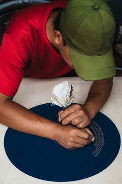 Sopsokha, Bhutan - 19 September 2025: View of a man in a red shirt and green cap intently embroidering on a navy blue canvas, crafting delicate patterns.