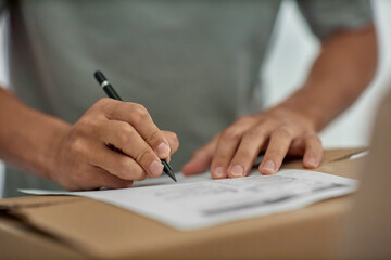 Man signing document on cardboard box, closeup of hands holding pen and writing, focusing on...