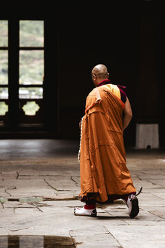 Paro, Bhutan - 17 September 2025: View of a lone monk, draped in vibrant orange robes, strides purposefully through the stone corridors of Rinpung Dzong, a scene of solemnity.