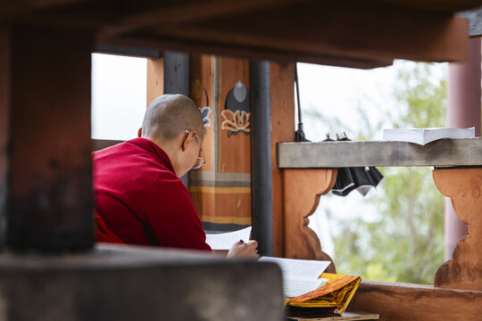 Punakha, Bhutan - 19 September 2025: View of a serene moment as a nun, draped in vibrant red, engrossed in study amidst the tranquil Wolakha Nunnery's wooden structures.