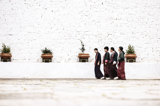 Paro, Bhutan - 17 September 2025: View of monks in traditional maroon robes traverse the courtyard before Rinpung Dzong's whitewashed walls, punctuated by potted greenery in terracotta pots.