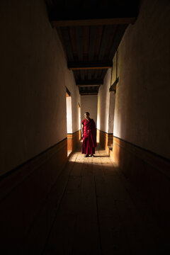 Punakha, Bhutan - 19 September 2025: View of a monk in vibrant red robes standing in a corridor, illuminated by soft light filtering through the windows, casting long shadows on the walls.