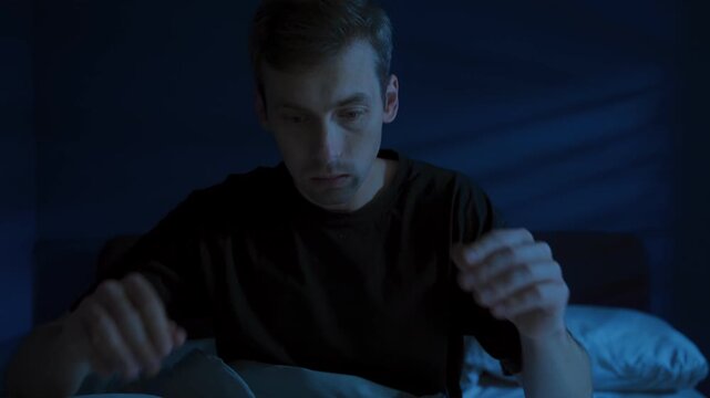 Young fearful man suddenly wakes up in the dark bedroom in the middle of the night in a panic attack because of nightmare due to night terrors and sleep disorder. Insomnia and sleep difficulty
