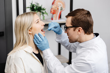 Obraz premium Doctor using inspection spatula to examine patient throat. ENT doctor doing throat exam of a woman. Patient opened her mouth to throat check-up