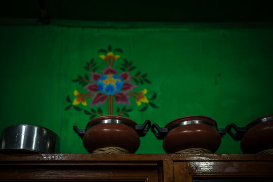 Ha, Bhutan - 25 September 2025: View of earthen pots resting on a shelf against a vibrant green wall adorned with a colorful, floral design.