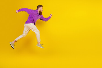 Fototapeta premium Energetic young man in purple hoodie leaps mid air against bright yellow background for a dynamic lifestyle and fitness oriented stock image