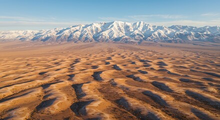 Vast Desert Dunes Meet Snow-Capped Mountains Under a Clear Blue Sky.
