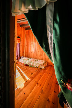 Ha, Bhutan - 26 September 2025: View of a simple bed bathed in golden sunlight streaming through a doorway, framed by rich green and white curtains against warm wooden walls.