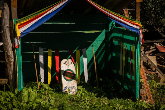 Ha, Bhutan - 26 September 2025: View of a small, shadowed green structure, adorned with colorful flags and a shield, nestled among lush greenery, creating a scene of cultural vibrancy.