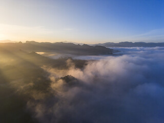Fototapeta premium Serene aerial view of mountain landscape at sunrise, with golden sunbeam and light piercing through morning fog. peaceful and beautiful natural scene above cloud
