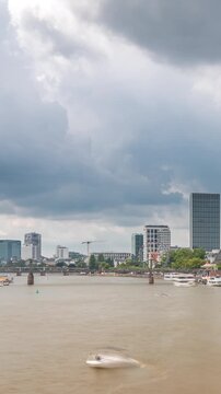 Hyperlapse of the historical Eiserner Steg (Iron Bridge) over the Main River in Frankfurt, Germany. Skyscrapers skyline and waterfront reflect in the water under a cloud-filled sky timelapse