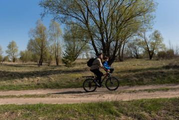 Father rides his little son on the handlebars of a bicycle in a meadow
