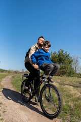 Father rides his little son on the handlebars of a bicycle in a meadow