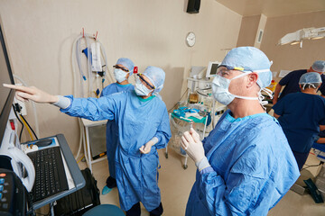 Surgeon, team and point at monitor with meeting, talk and emergency room with insight at hospital. Doctors, medical staff and people with scan for feedback, solution or face mask in theater at clinic