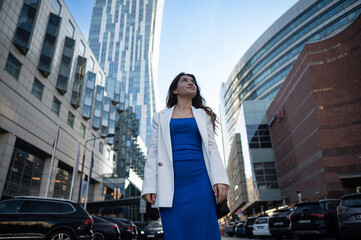 A young ambitious girl walks the streets among the skyscrapers and cars in a big city.