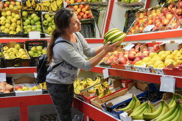 A woman selects fruit at a market, assessing its quality, holding bananas in her hand. Organic produce on display at a fruit store, sale