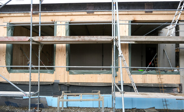 Baustelle in Modulbauweise mit eingesetzten Holzelementen und sichtbaren Fenster&ouml;ffnungen w&auml;hrend der Montage der Module im Erdgeschoss, Ger&uuml;st