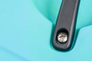Close up detail of metal screw and black plastic handle on turquoise background. macro view of fastener and industrial component showing connection and assembly