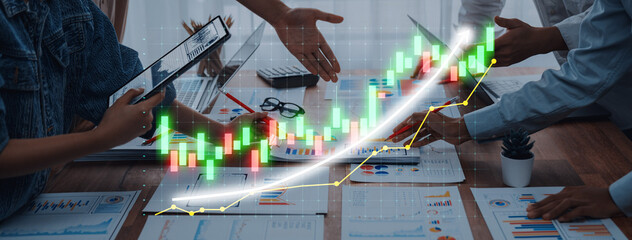 A diverse business team collaborates on financial growth strategies with charts, laptops, and data visualizations on a wooden table in an office setting. Axiom