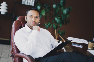 Confident businessman sits in a modern office chair with a clipboard and coffee in a professional stylish loft setting