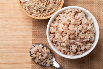 Cooked Thai brown rice in a bowl with spoon on wooden background, Healthy eating, Top view