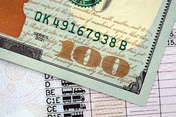 Obraz premium Hundred dollar bill on US driver license close up. Concept of driving lessons or automobile taxpaying