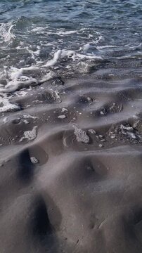 Calming ocean tide with white foam gently washing over a beautiful, dark, lumpy sand beach. Serene seaside scenery in slow motion