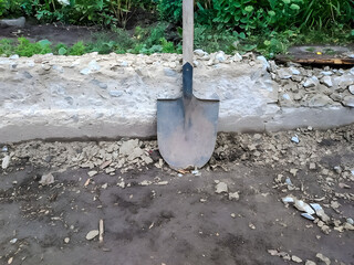Shovel leaning against a concrete wall in a garden setting