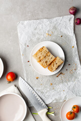 overhead view of slices of onion and scallion focaccia on parchment paper, top view of airy bubbly onion focaccia on a cement countertop