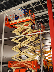 Construction workers installing ceiling panels using a scissor lift