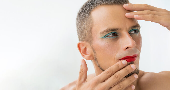 portrait of a feminine gay man with makeup and cosmetics on face. Handsome transgender male with red lipstick on lips and mascara on eyes on white background with copy space
