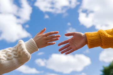 Reaching Out: Two pairs of hands, one with long sleeve in white, the other in yellow sleeve, reach toward each other against a backdrop of a vibrant blue sky with fluffy clouds.