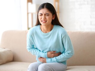 Woman Sitting on Couch Holding Stomach in Pain - Health Issues, Discomfort, and Wellbeing
