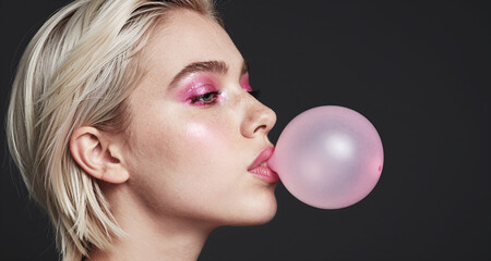 Ritratto primo piano volto di elegante e affascinante ragazza che fa una bolla con una gomma da masticare, su fondale scuro