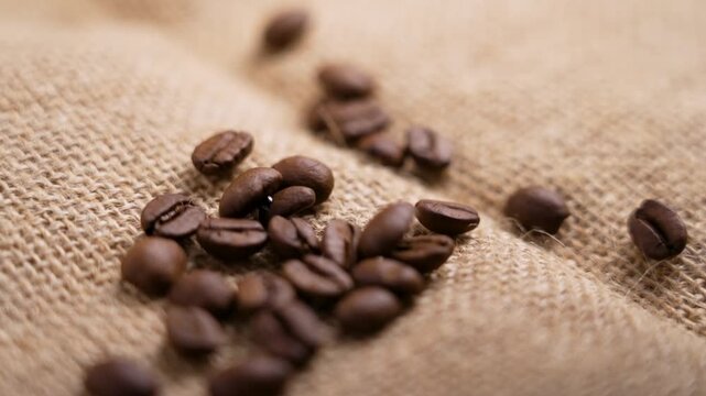 Fresh roasted Arabica coffee beans falling onto rough sack cloth in slow motion. Aromatic invigorating ingredient of morning beverage