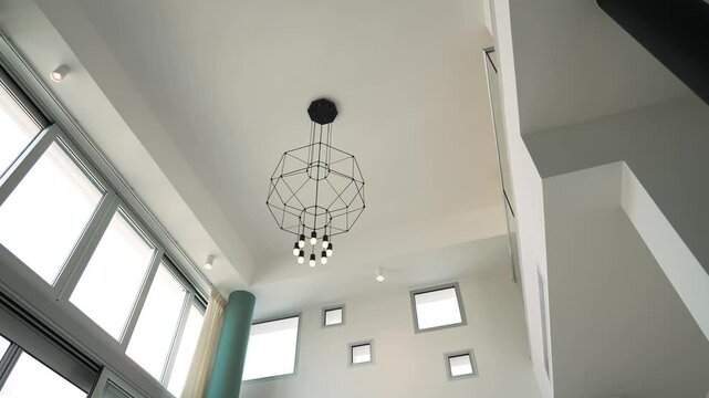 Modern loft interior ceiling with chandelier, tall windows geometric window cutouts, soft daylight flooding white walls, teal column, airy minimalist ambience,
