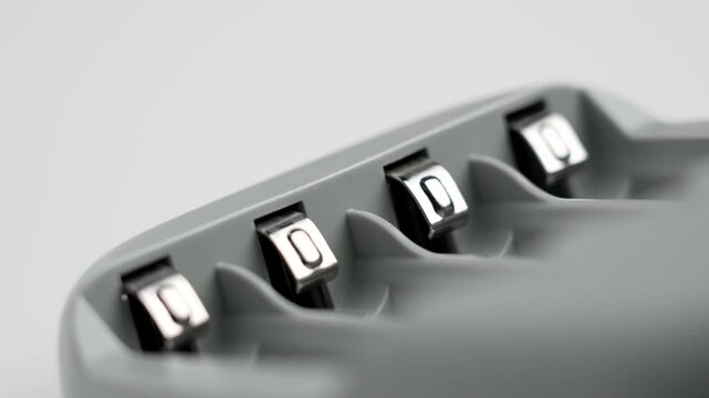 Household alkaline AAA battery charging block with shiny metal contacts on white table close up