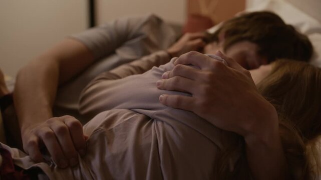 Young Caucasian couple lying in bed together, sharing warm and intimate moment while cuddling and touching each other tenderly, enjoying closeness and romantic connection