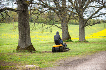 Spring mowing scene with man on garden tractor in Latvia