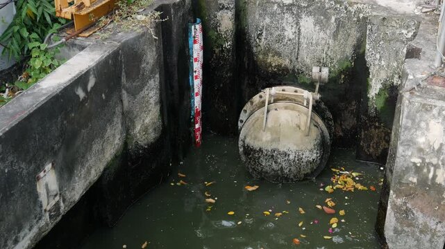 Drainage system with metal flap valve and water level gauge at concrete canal, flood control and sewage management concept in urban area.