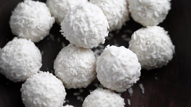 White cream truffles covered in coconut flakes falling into a wooden bowl. Slow motion