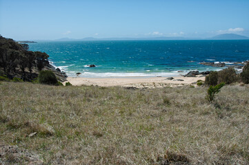Remote Tasmanian east coast bay with empty beach, blue sea and distant mountains, perfect for adventure travel campaigns, ecotourism promotions and destination editorials.