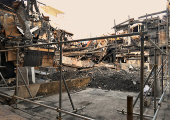 大規模火災によって崩れ落ちた建物の瓦礫と立ち入り規制のフェンス・商店街の火事跡、災害復旧と解体工事の現場風景 © taka