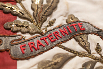 D&eacute;tail d'un vieux drapeau fran&ccedil;ais sur lequel est &eacute;crit le mot " Fraternit&eacute; " en rouge.