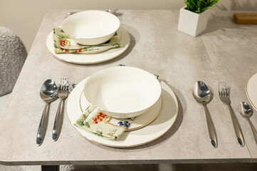 Elegant table setting with white bowls and silver cutlery on neutral surface