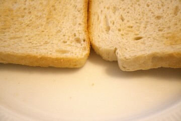 Two slices of plain toast arranged on a white plate in a close-up view, showing the textured surface in natural condition. Minimal styling ideal for breakfast concepts.