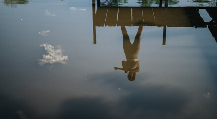 A peaceful scene capturing a reflection of a person by a dock in still water. The serene atmosphere...