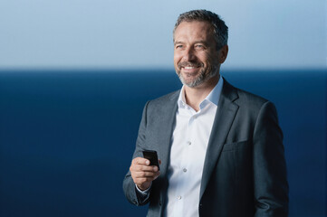 Smiling man in business suit holding smartphone against blue background